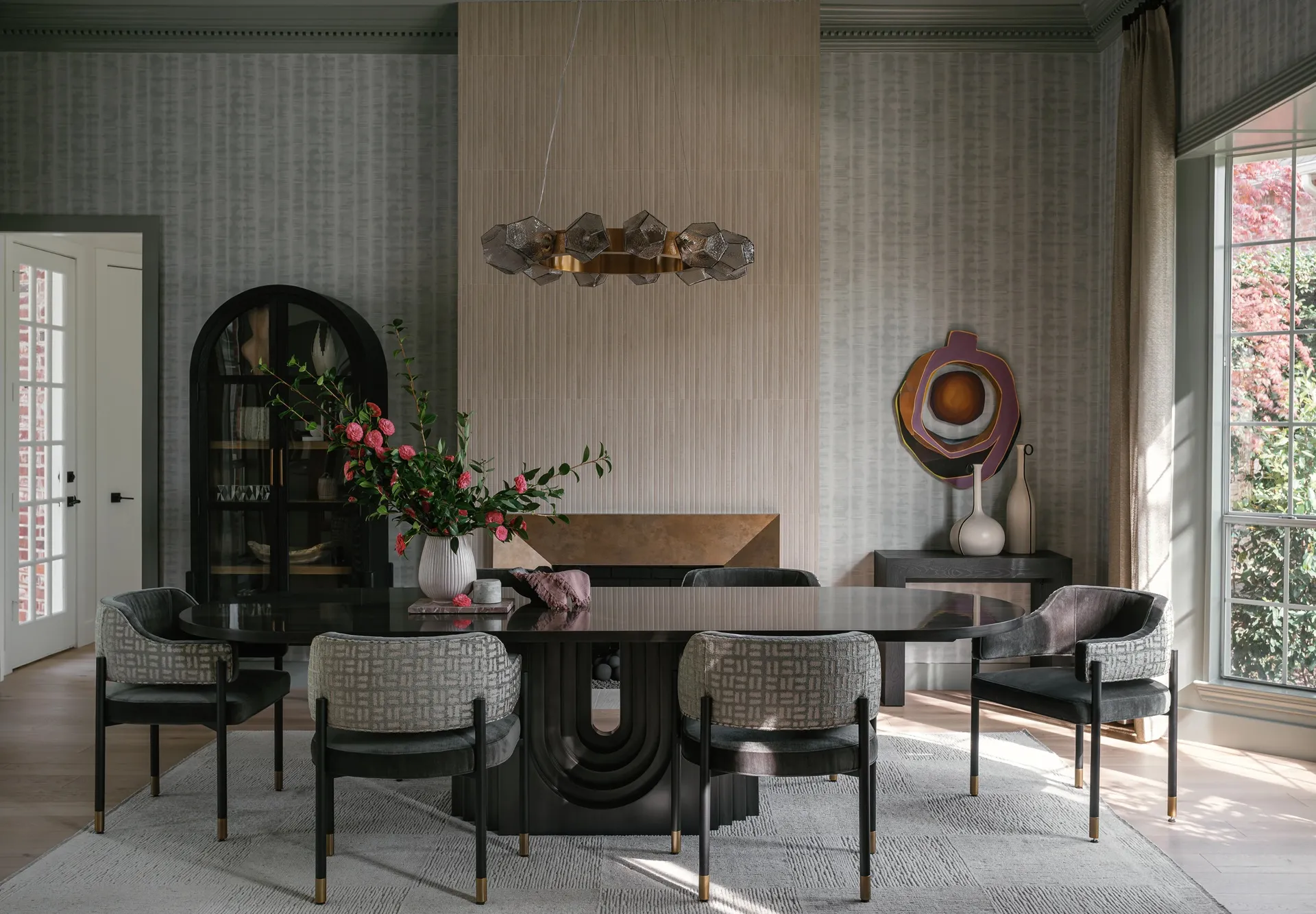 Dining room with an oval lacquered table, upholstered armchairs, a faceted glass chandelier, and a floral centerpiece.