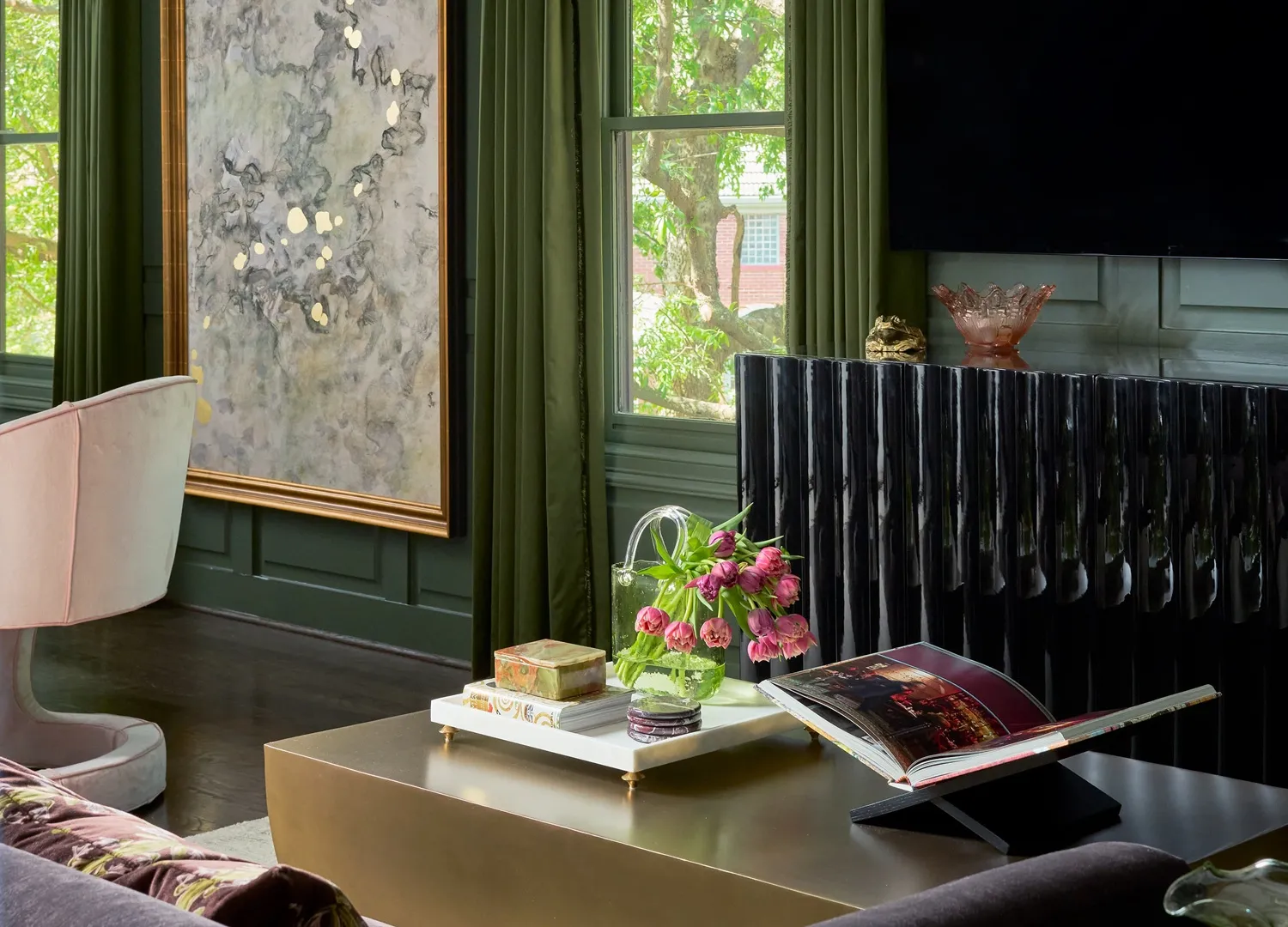 Green lounge and bar area with a patterned marble backsplash, brass shelving and pink velvet chairs around a round marble table
