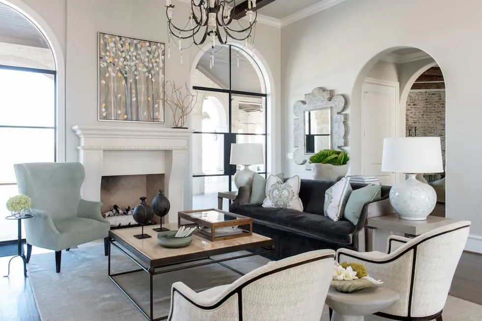 living room with a white fireplace, an iron chandelier, a velvet sofa and an arched steel-framed door.