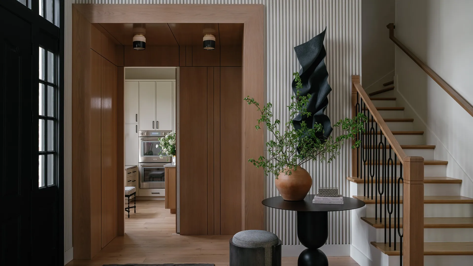 Kitchen seen through a wooden arch, with a blue marble island, attached walnut dining table and a pendant light over white cabinetry