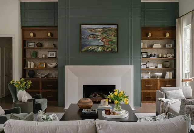 Dining room with a black table and grey upholstered chairs, a linear brass chandelier, round mirror over a sideboard and hand painted walls
