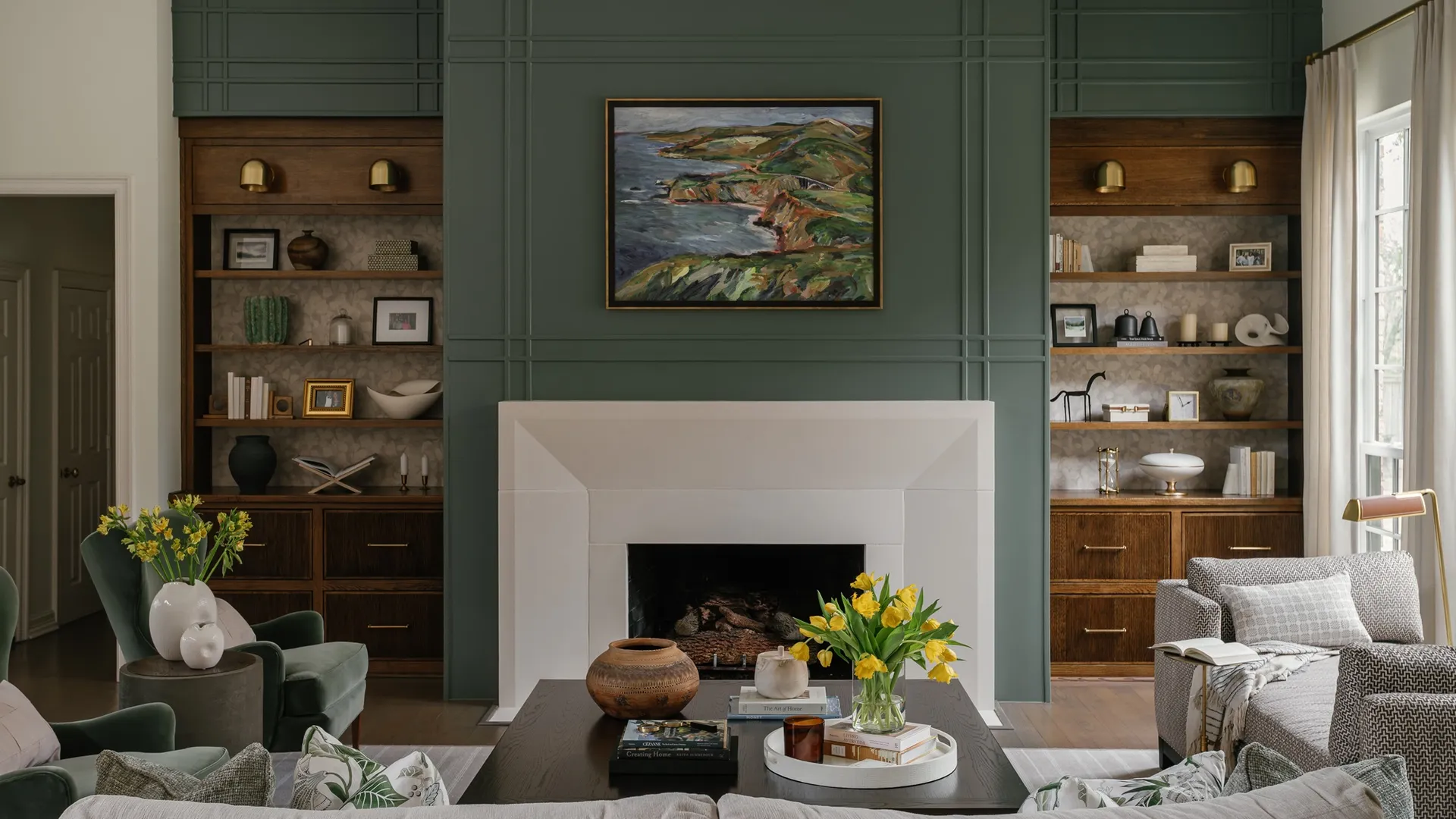 Living room with sage green panelled walls, wooden built-in shelving, a limestone fireplace and yellow tulips on a dark coffee table