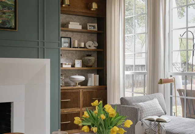 Living room with sage green panelled walls, wooden built-in shelving, a limestone fireplace and yellow tulips on a dark coffee table