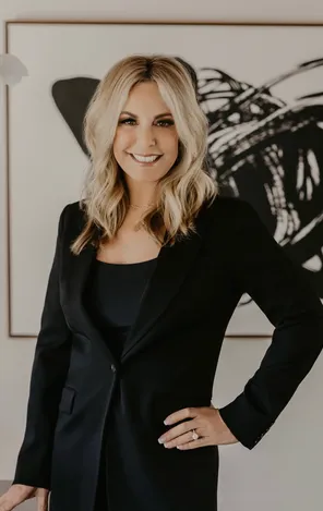 Traci Connell smiling in a black blazer in front of a framed abstract artwork.