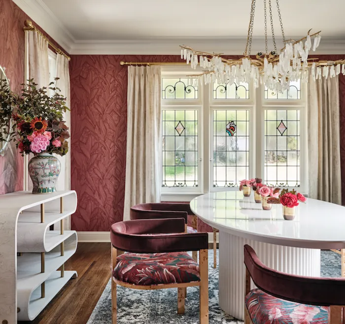 contemporary dining room with a sculptural white table, velvet chairs, and burgundy floral wallpaper.