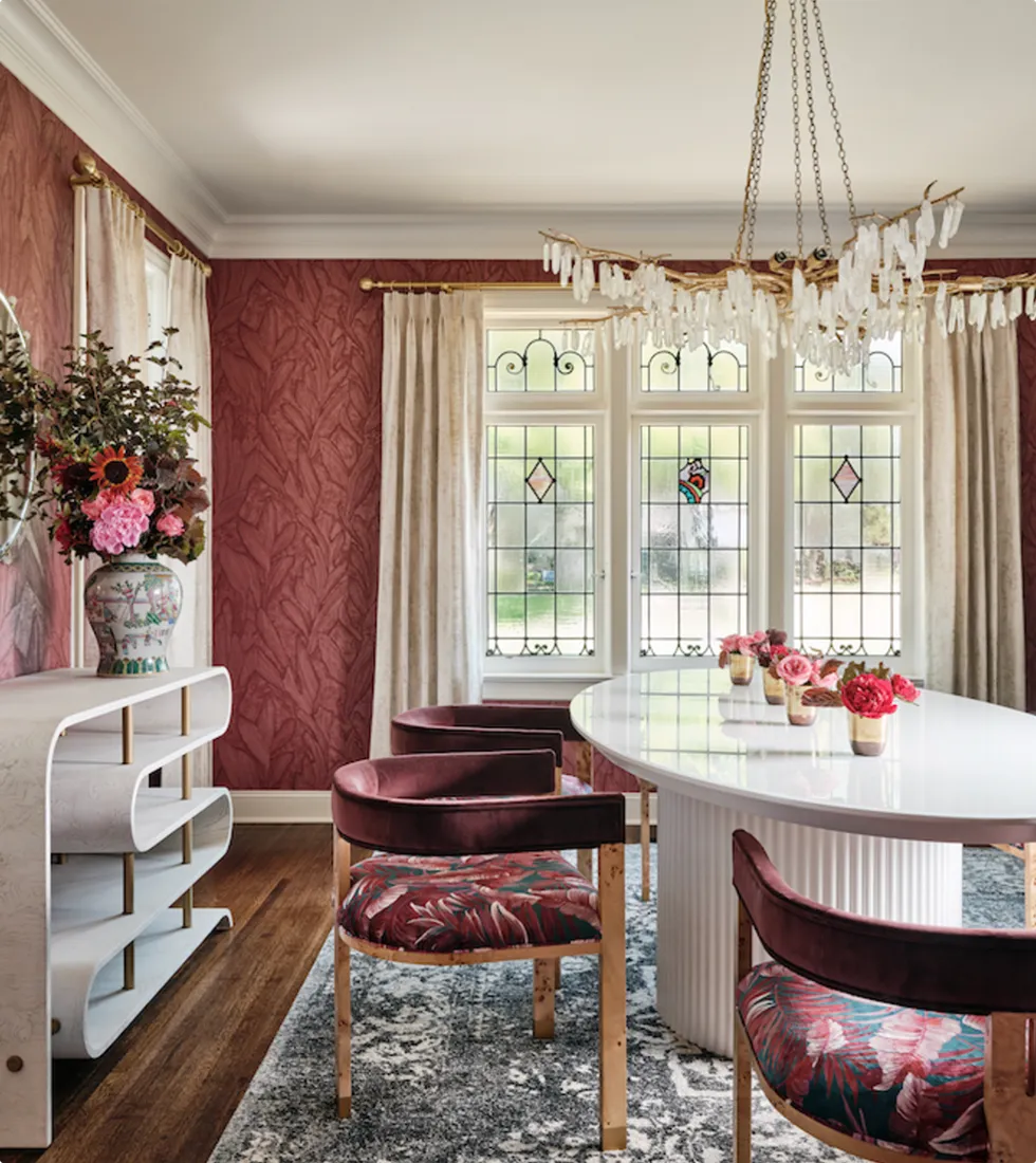 contemporary dining room with a sculptural white table, velvet chairs, and burgundy floral wallpaper.